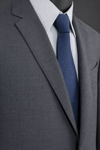 Close-up of a grey suit jacket with notched lapels and a blue tie against a charcoal studio background